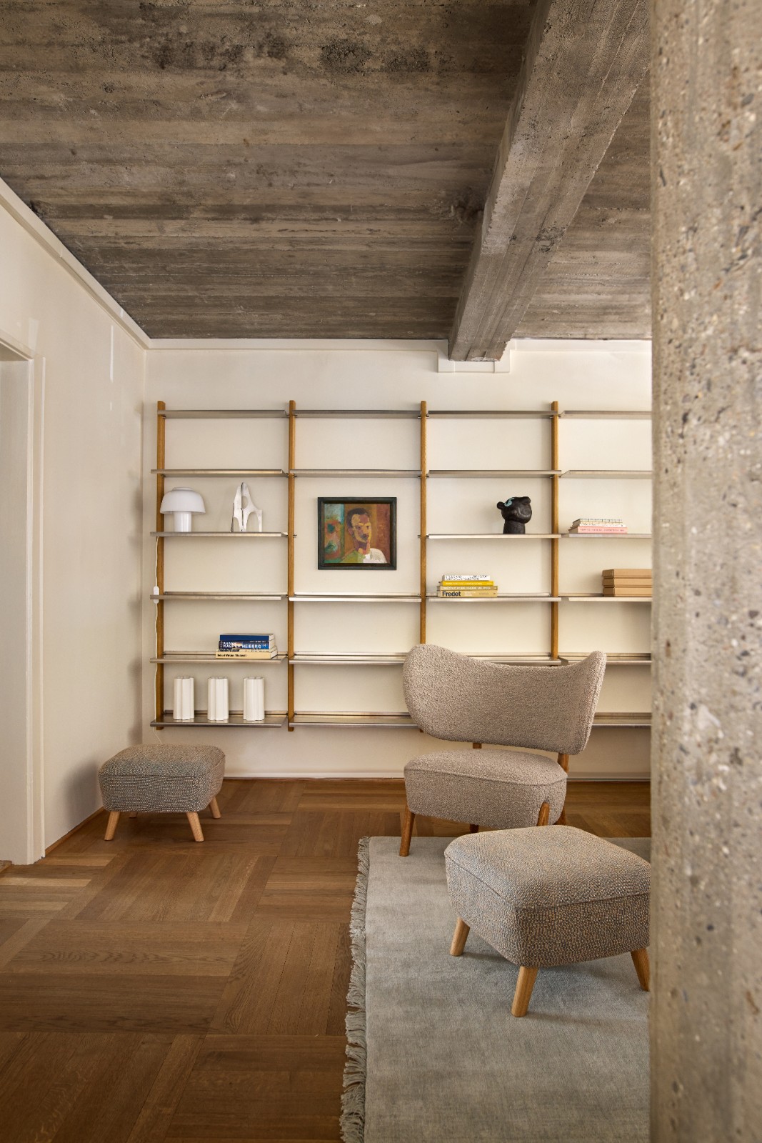 TMBO Lounge Chair and pouf in beige upholstery in front of a MOD Shelving System under a concrete ceiling