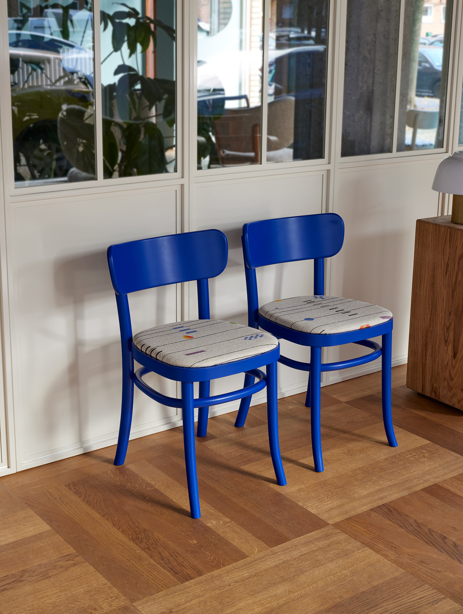 Two blue MZO Chairs with patterned seat pads against a white wall beside a glass partition