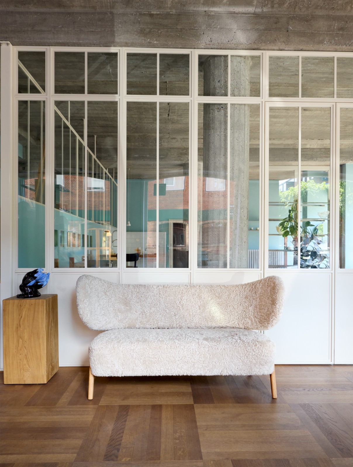 TMBO Sofa in cream sheepskin in front of a glass partition wall with an oak plinth