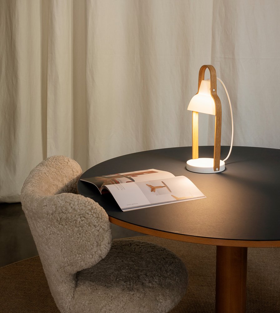 16PLUS Table Lamp glowing on a round table beside a sheepskin lounge chair