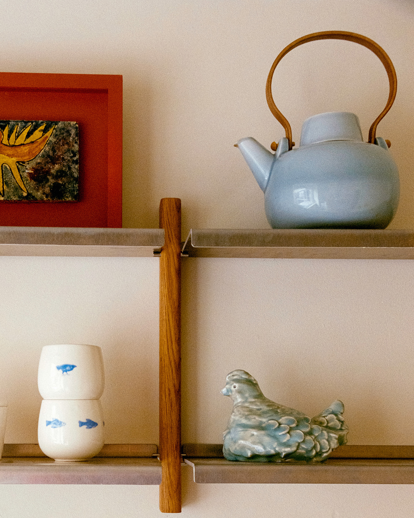 MOD Shelving System in oak and aluminium with books, a ceramic vase and a lit shelf lamp above a man writing at an oak desk