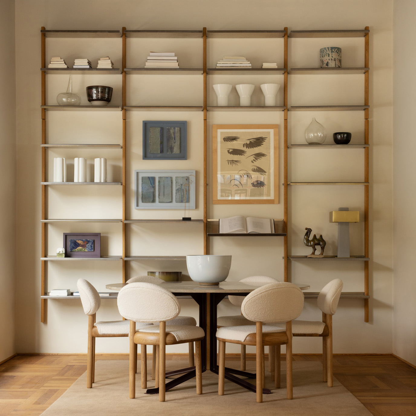 MOD shelving system styled with books, vases and artwork behind a round dining table with upholstered chairs in the Mazo showroom