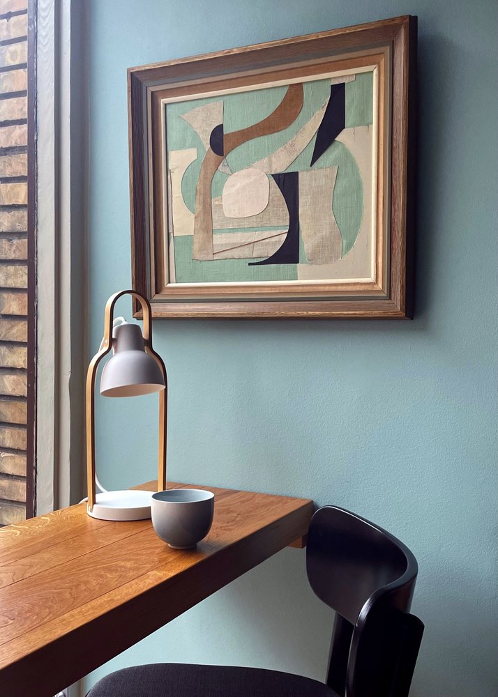 16PLUS Table Lamp in grey on a wooden desk beneath a framed artwork