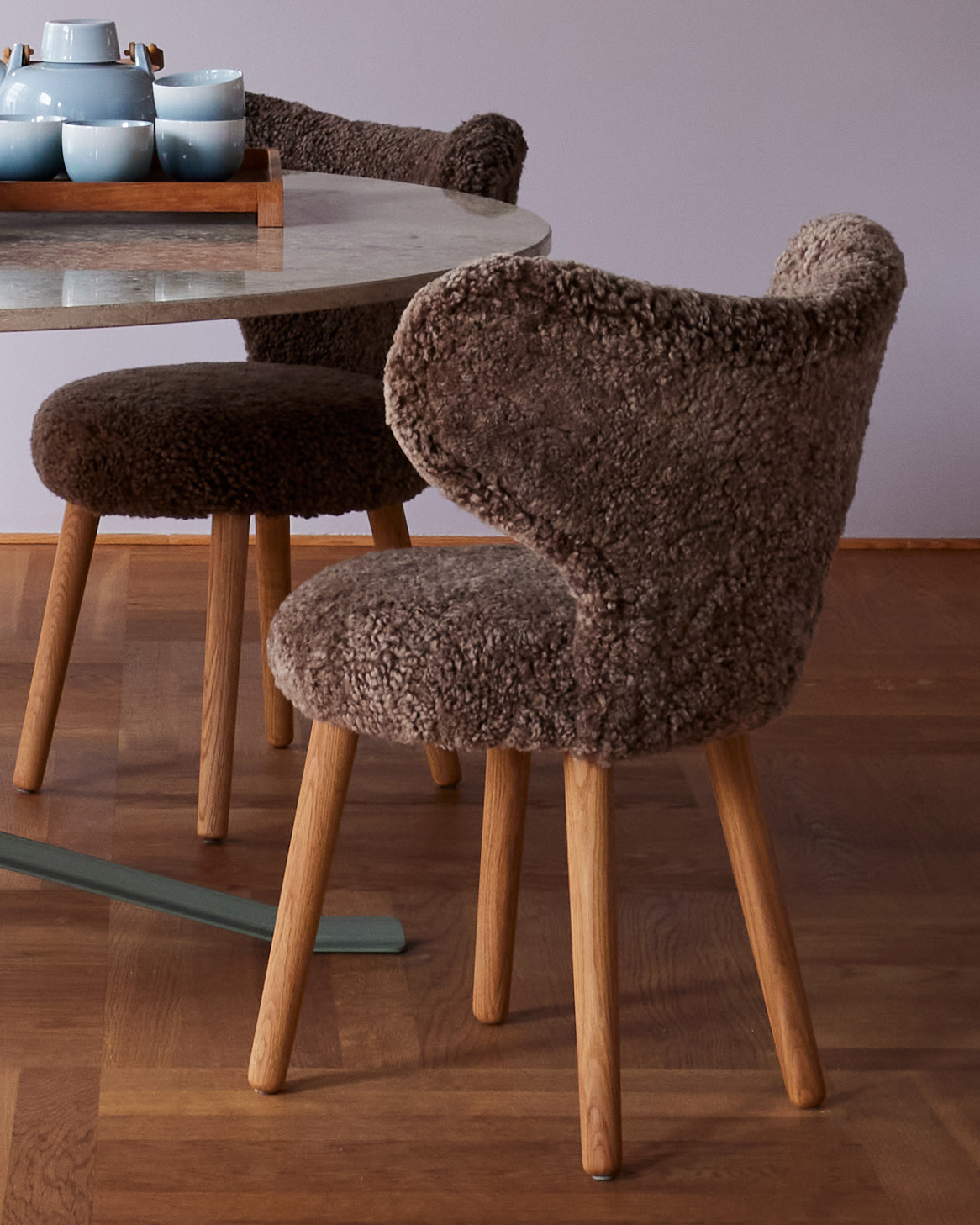 WNG chairs in brown shearling beside a round marble table with a blue tea set in the Mazo showroom