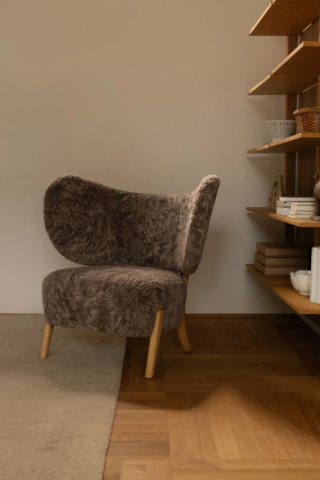 TMBO Lounge Chair in brown sheepskin with oak legs beside an oak shelving unit