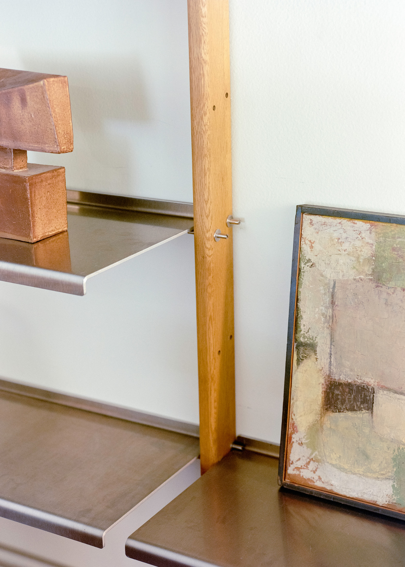 Detail of a MOD Shelving System oak upright with aluminium shelf brackets, a terracotta sculpture and a framed abstract painting