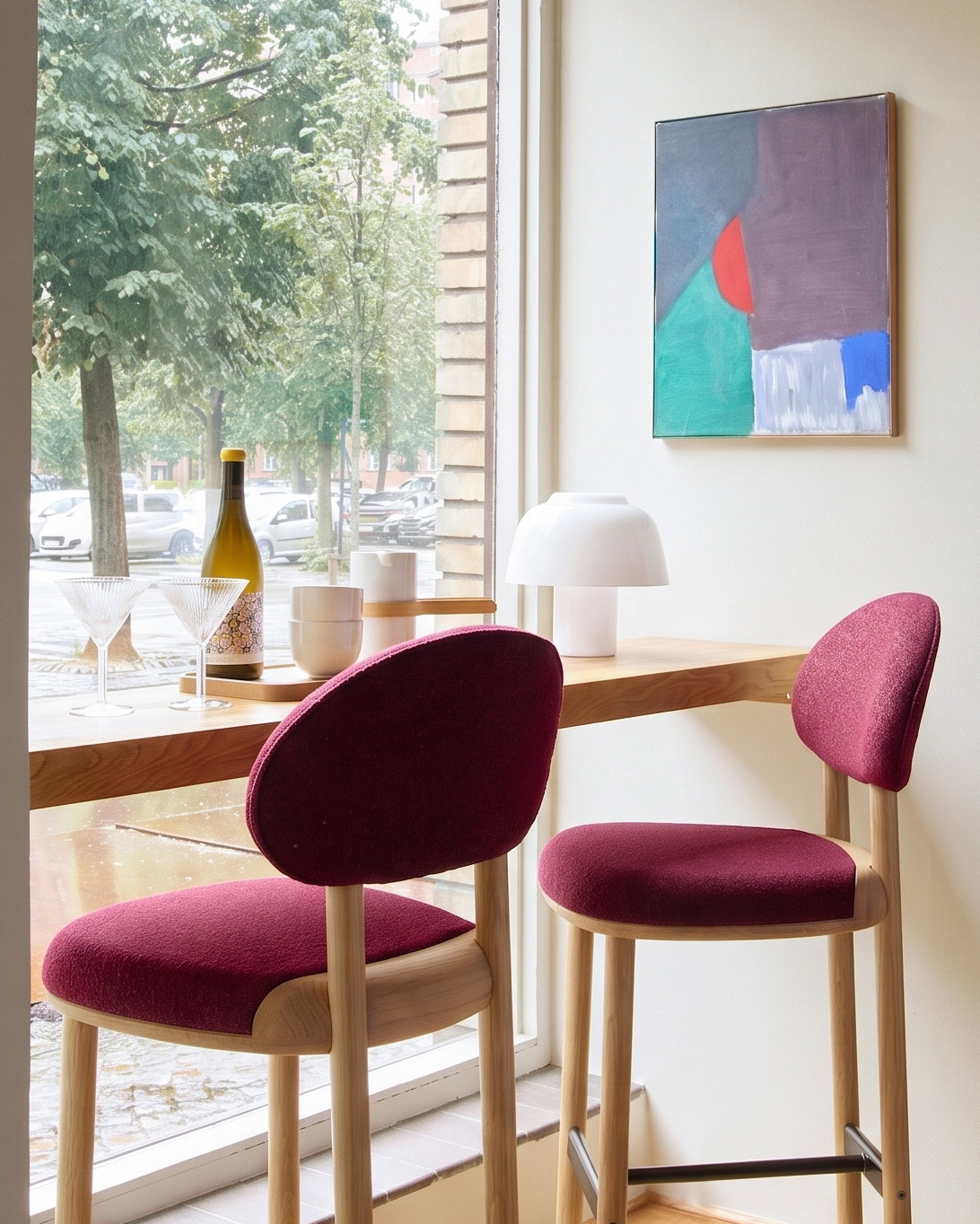 Two MAG Counter Chairs in burgundy upholstery at an oak window bar with a painting above