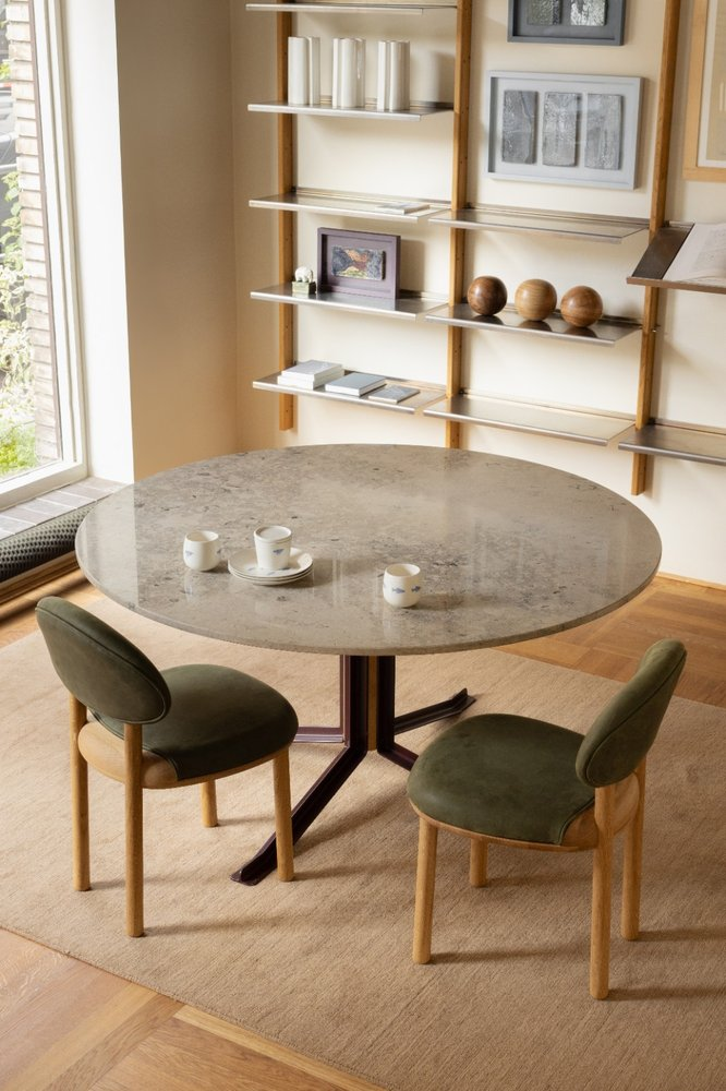 Two green MAG Dining Chairs at a round marble dining table with MOD Shelving System behind