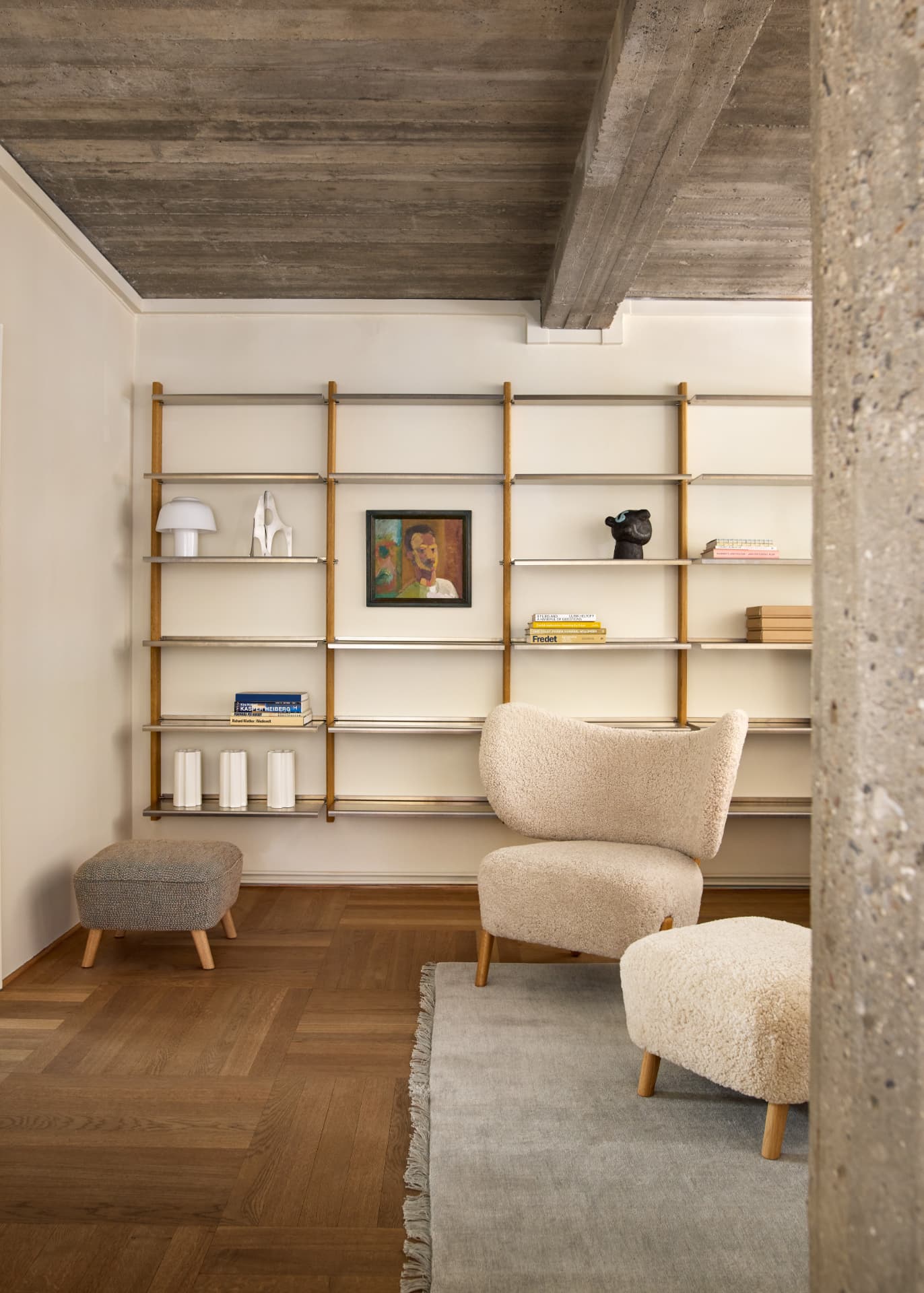 MOD Shelving System in oak and aluminium in a living room with a bouclé wingback chair, a pouf and a striped ottoman