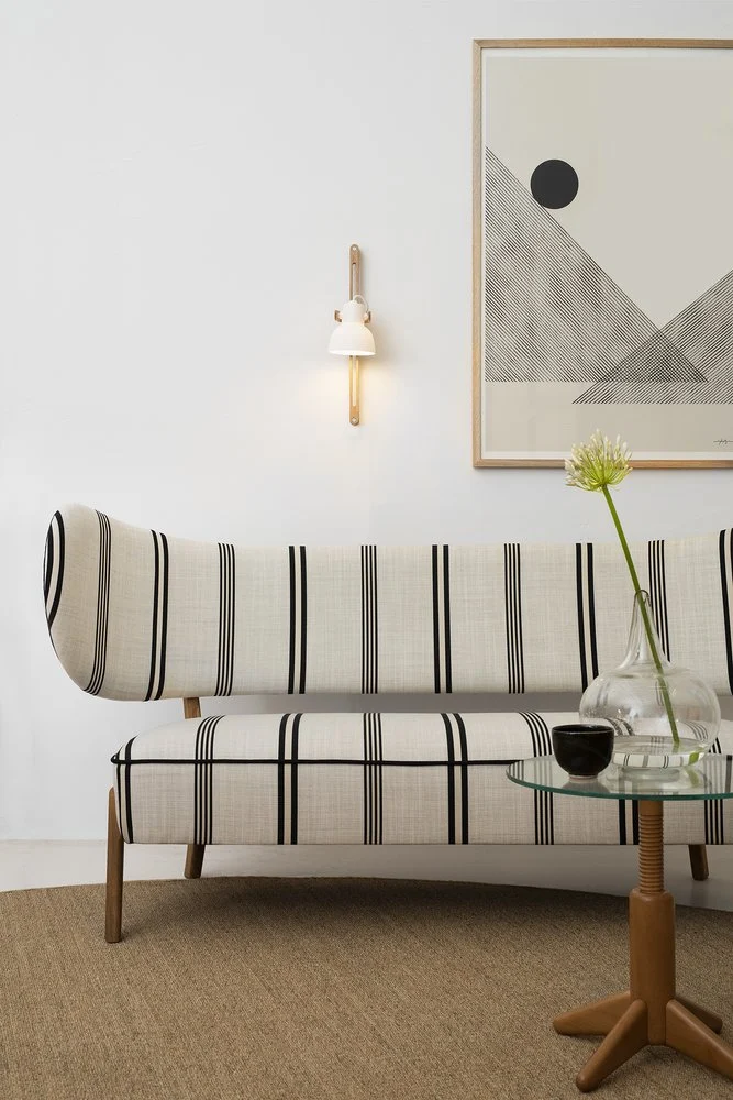 16PLUS Wall Lamp Adjustable above a striped sofa beside a glass side table