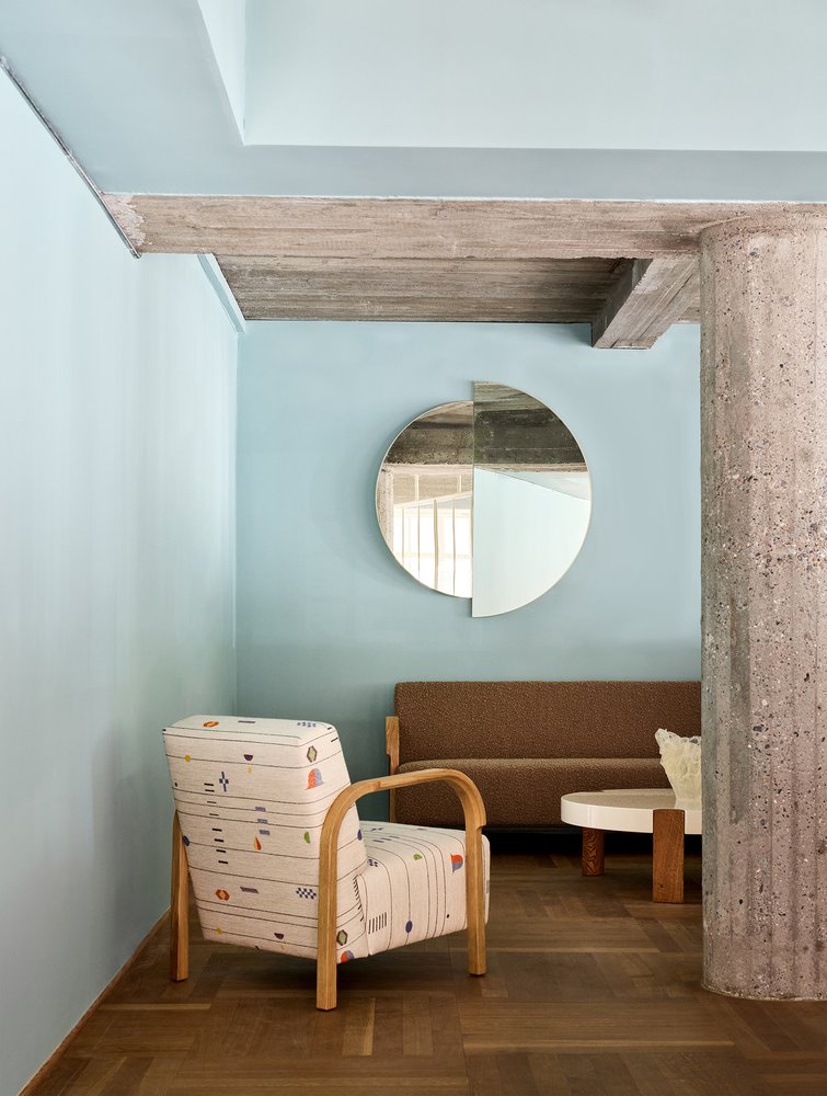 RAE Mirror O120 on a light blue wall above a patterned lounge chair and brown sofa