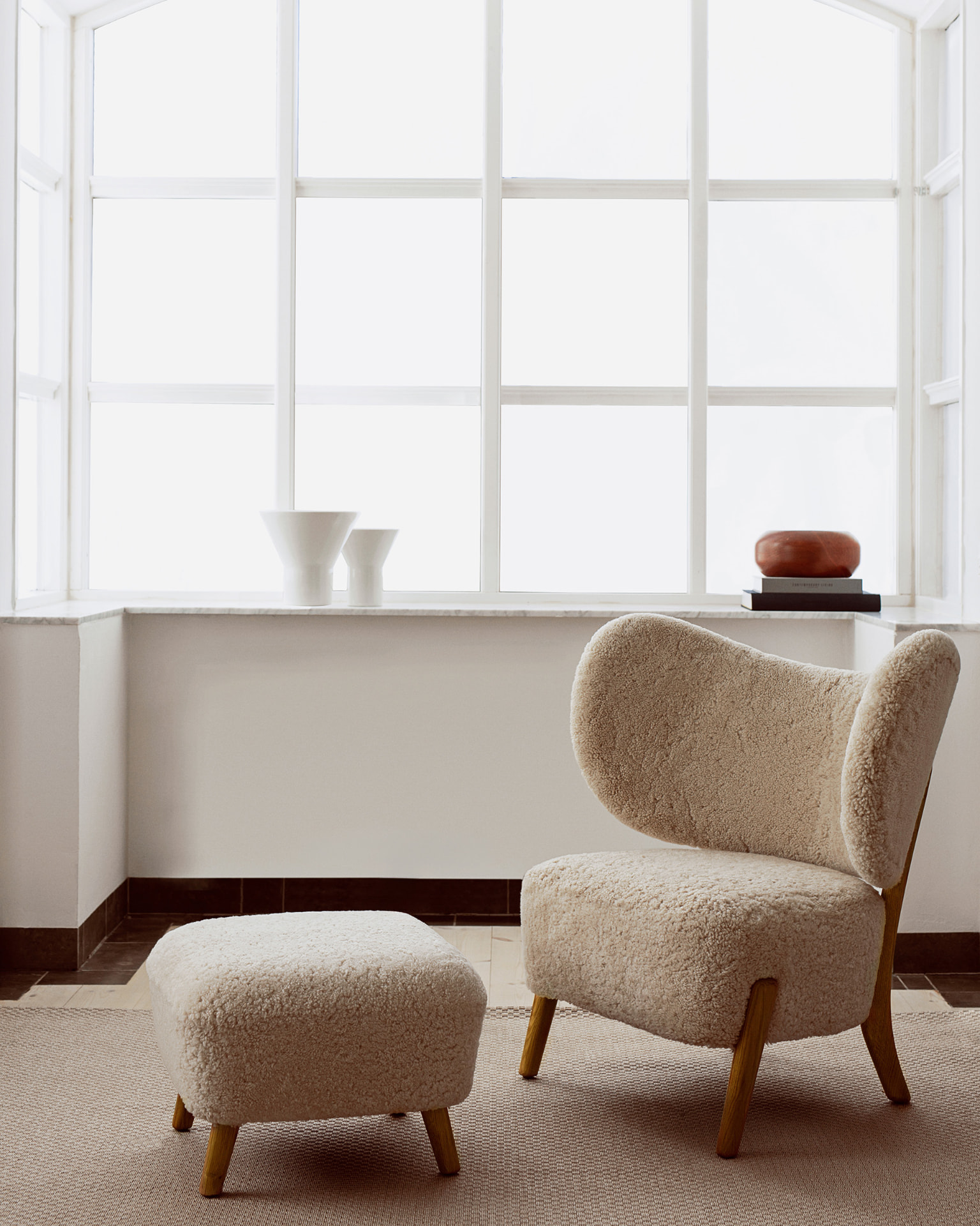 TMBO Lounge Chair with pouf in cream sheepskin in front of bright bay windows with ceramics on the sill