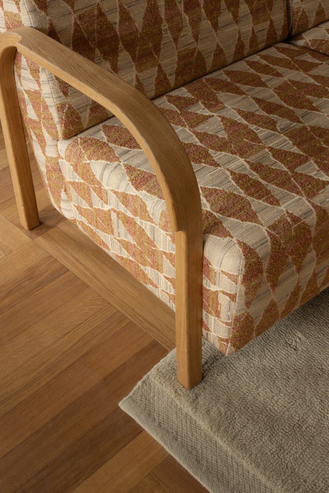 Detail of the ARCH 3 Seater Sofa in orange patterned upholstery with curved oak armrest