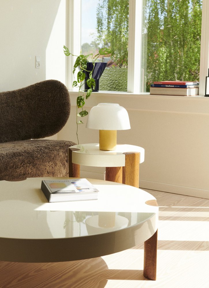 YUKI Lamp Olive on a round side table beside a sheepskin armchair by a bright window
