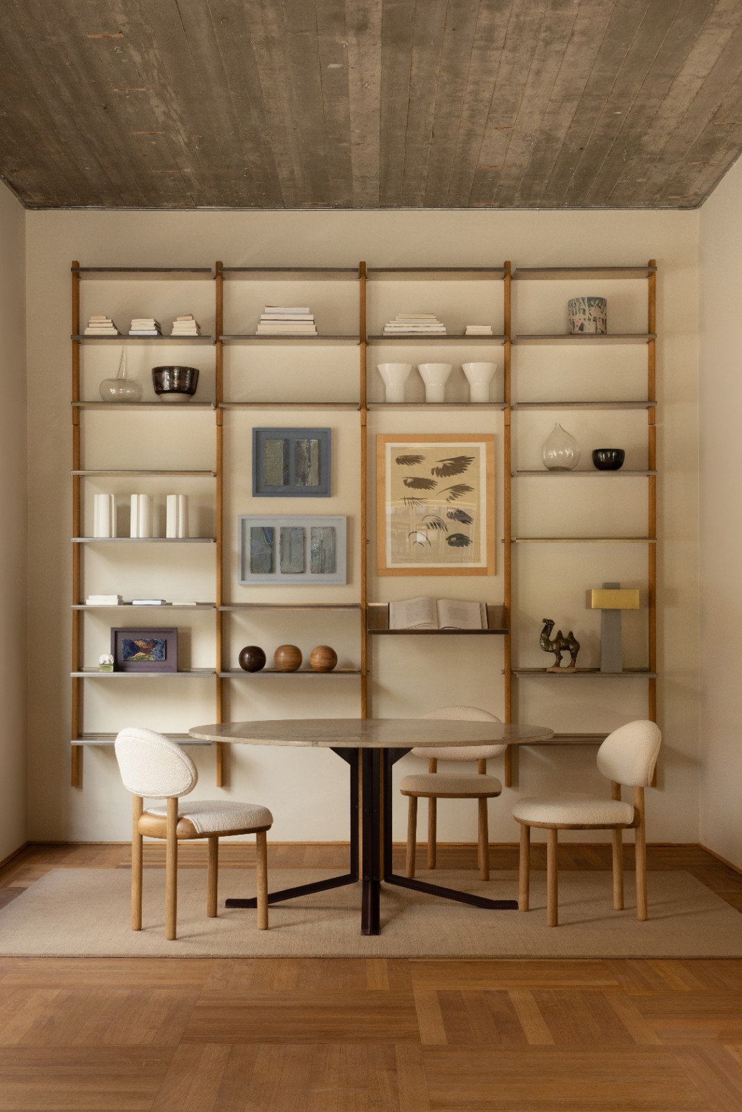 MOD Shelving System in oak and aluminium behind a round dining table with bouclé chairs