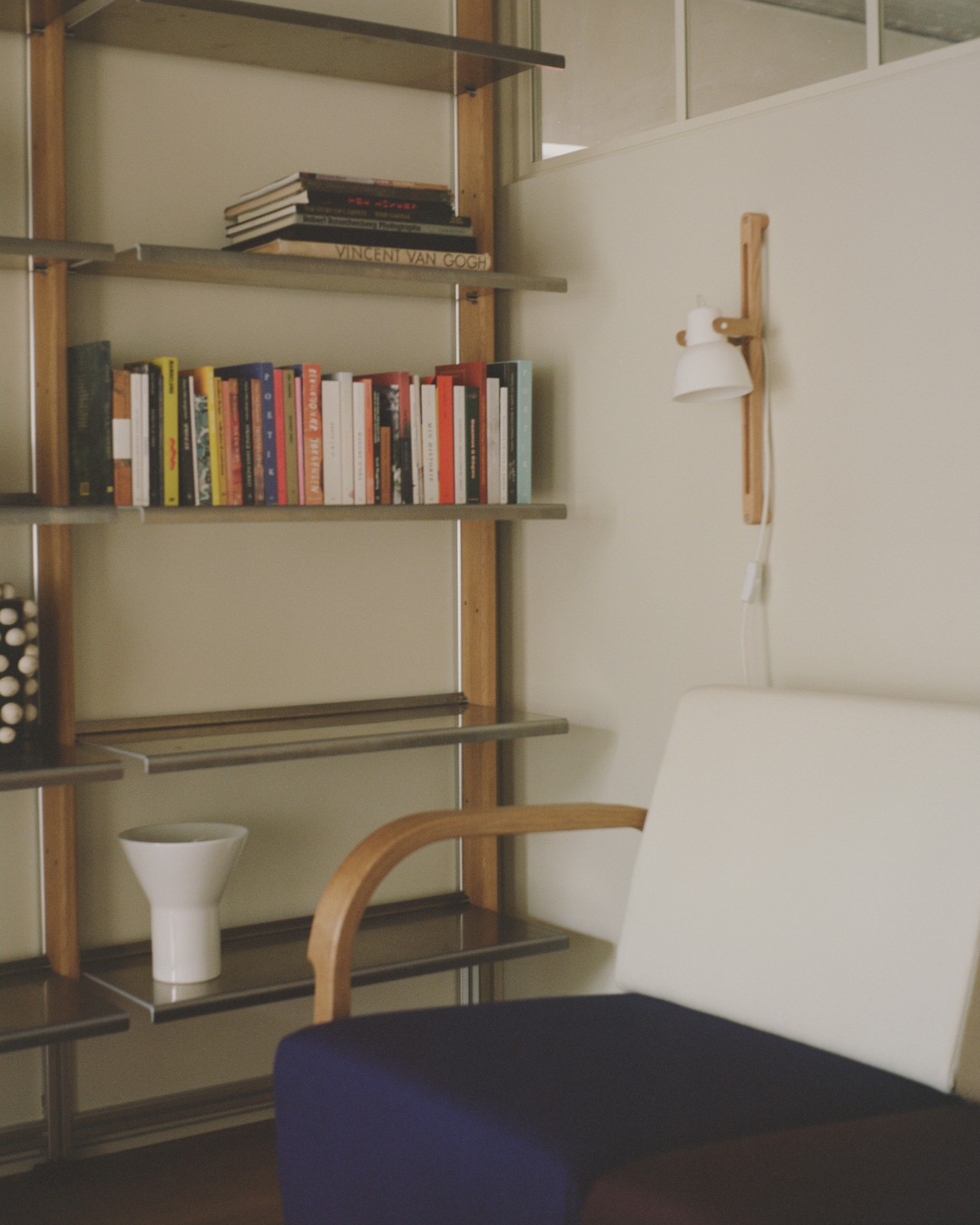 MOD Shelving System in oak and aluminium with books beside a reading chair and a wall lamp