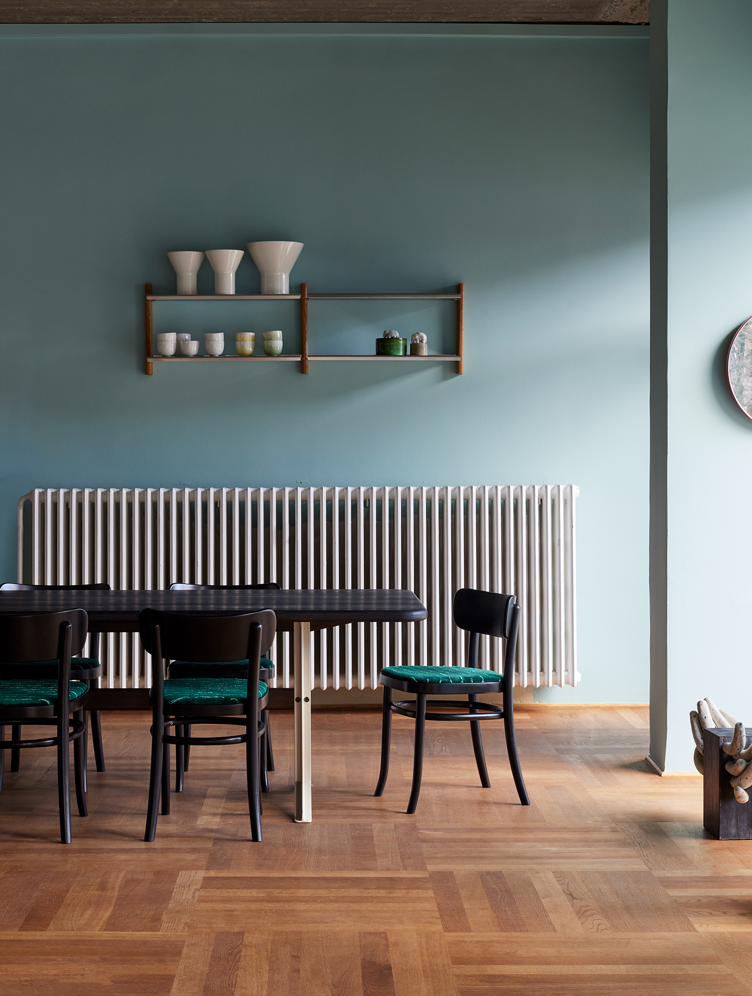 Black MZO Chairs with green velvet seat pads at a dark dining table in front of a radiator