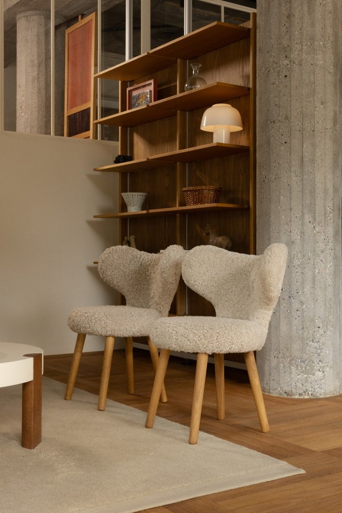 Two WNG Chairs in white sheepskin beside a walnut shelving unit and concrete column