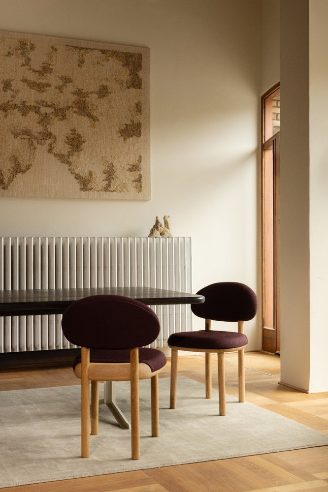 Two burgundy MAG Dining Chairs at a dark dining table beneath a large tapestry