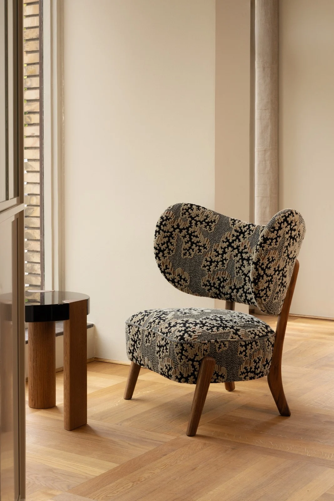 TMBO Lounge Chair in patterned upholstery with walnut legs by a window with an oak side table