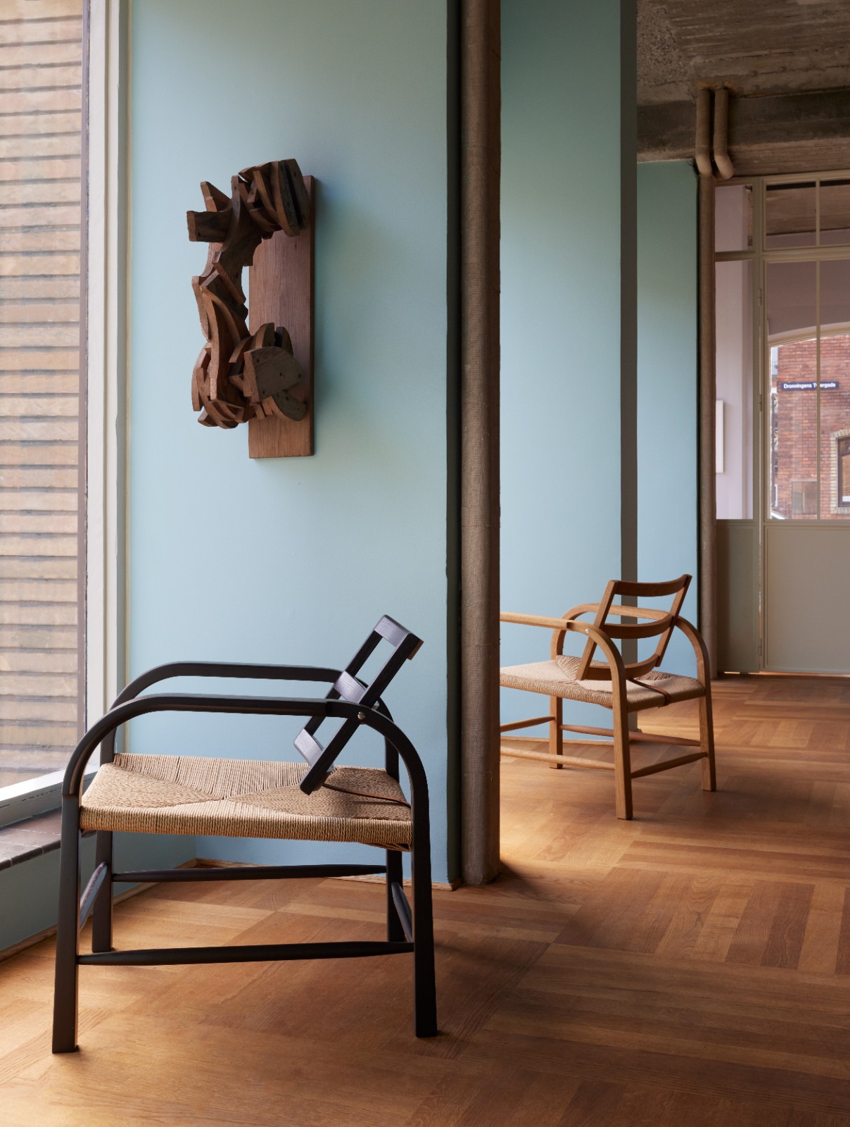 Two chairs beside a light blue wall with a wooden wall sculpture