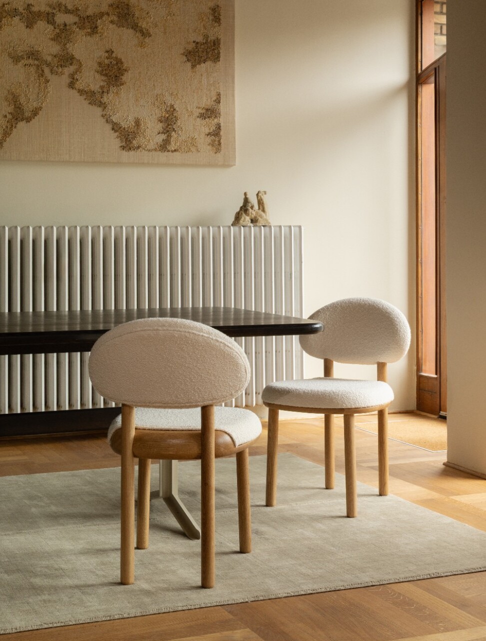 Two bouclé chairs with oak legs around a dark dining table in a warm dining room