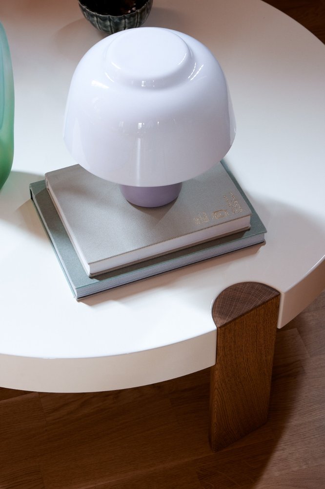 YUKI Lamp with lilac base resting on books on a white round coffee table with oak leg