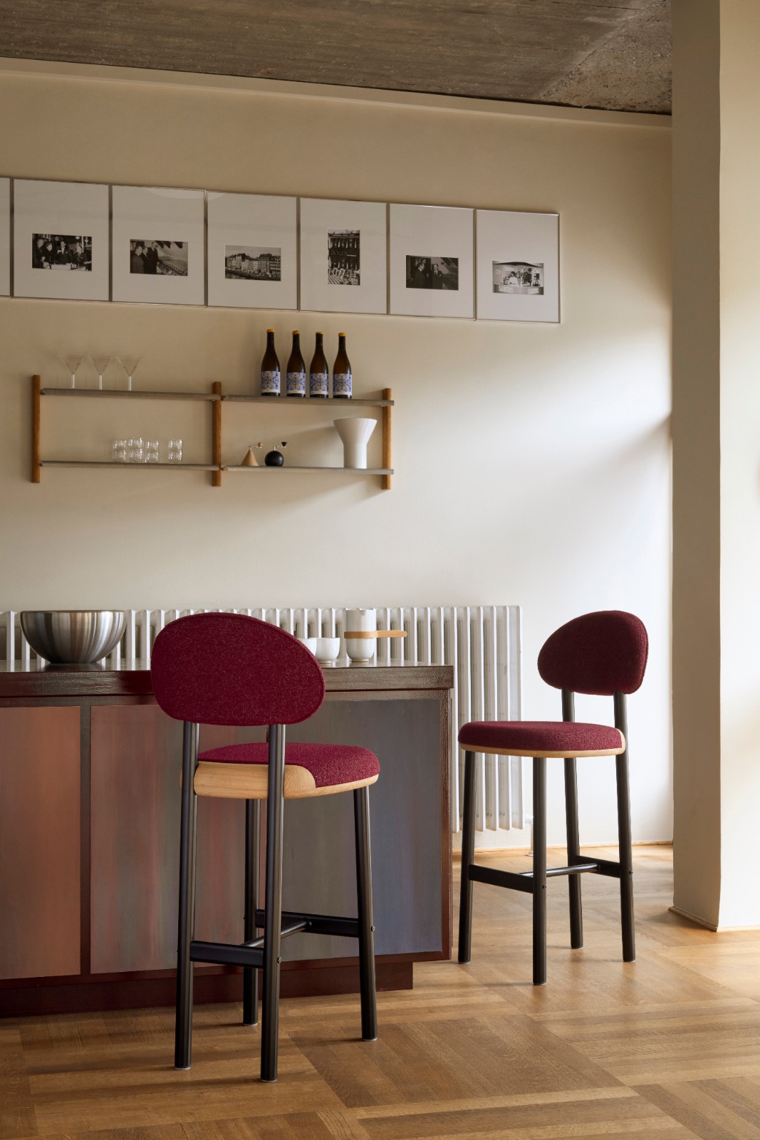 Two MAG Barstools in burgundy upholstery at a dark bar counter with a radiator and framed photographs behind