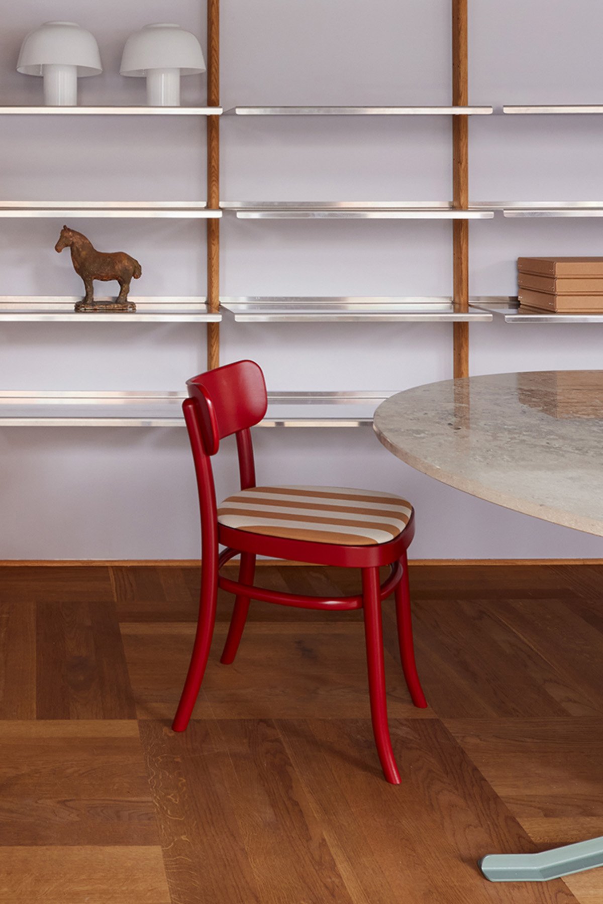 Red MZO Chair with striped seat pad beside a round marble table and a shelving system
