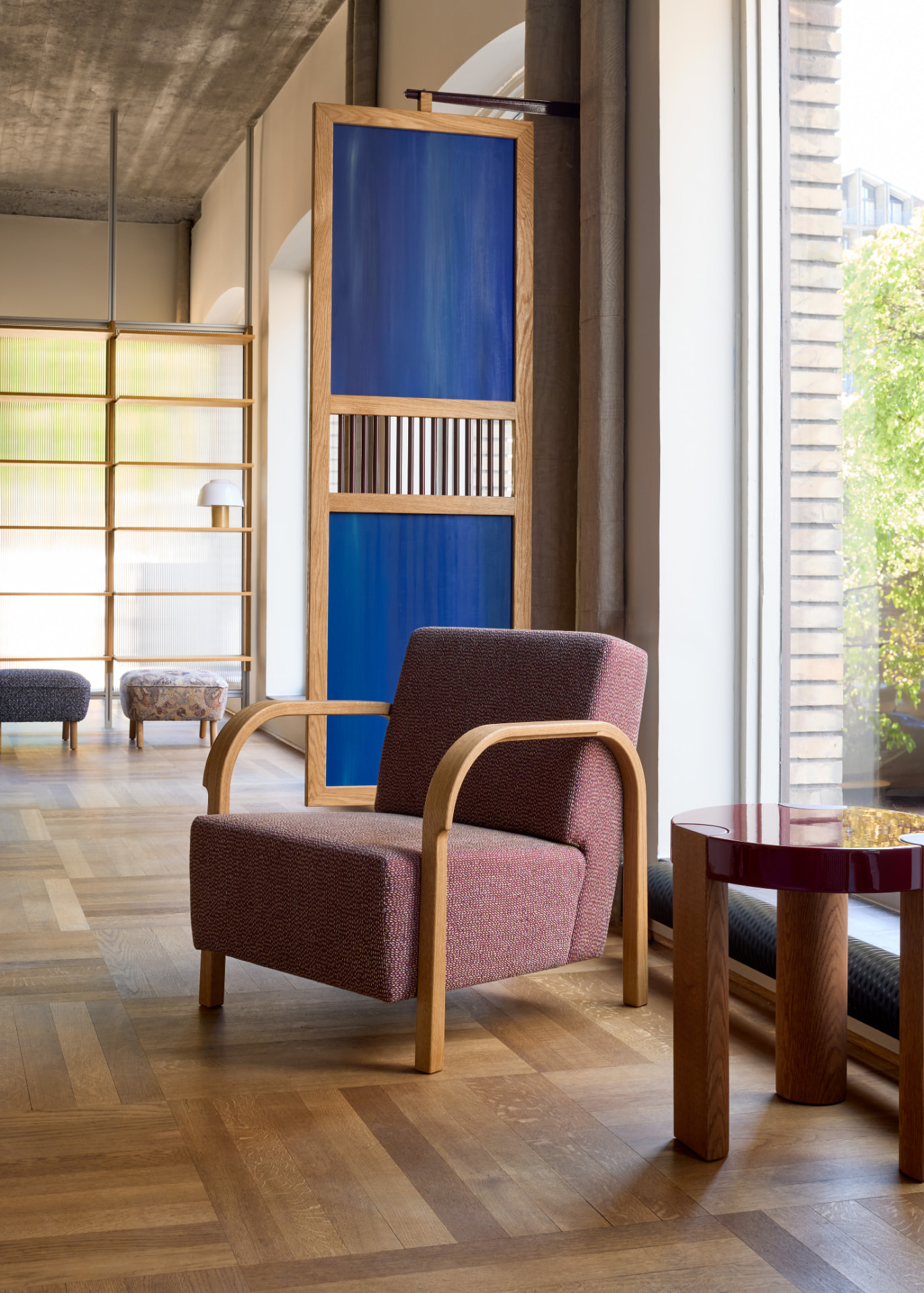 Arch Lounge Chair in maroon upholstery beside a large window in the showroom