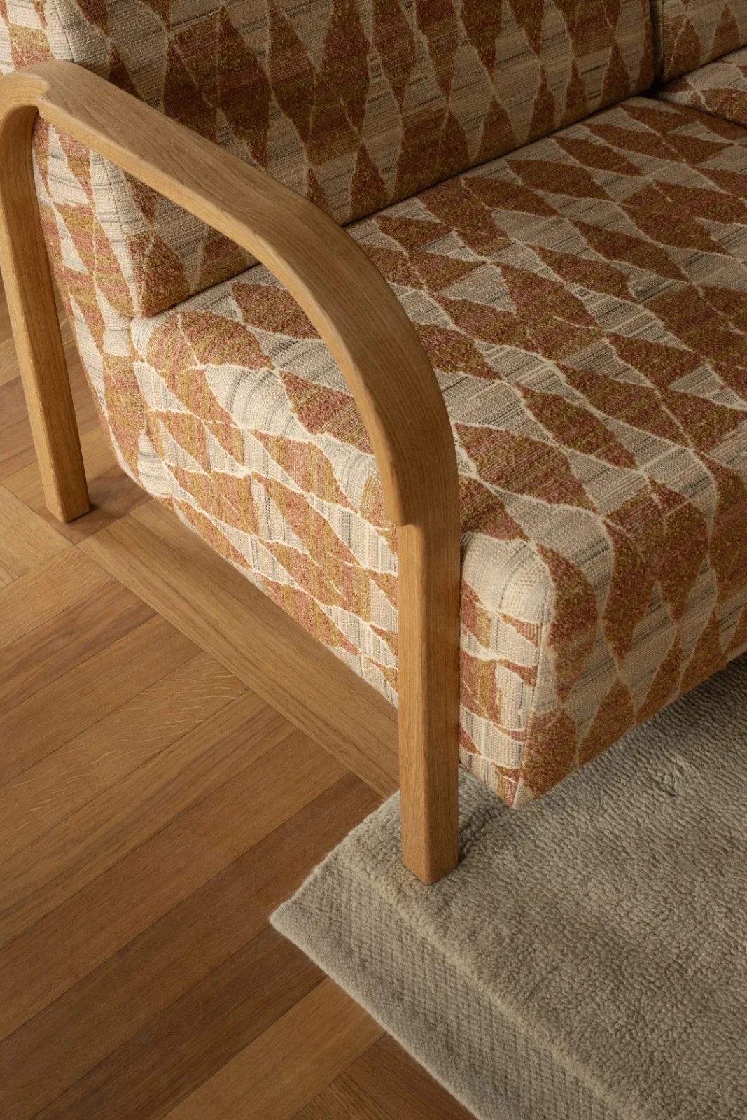 Detail of the ARCH 2 Seater Sofa in orange patterned upholstery with curved oak armrest