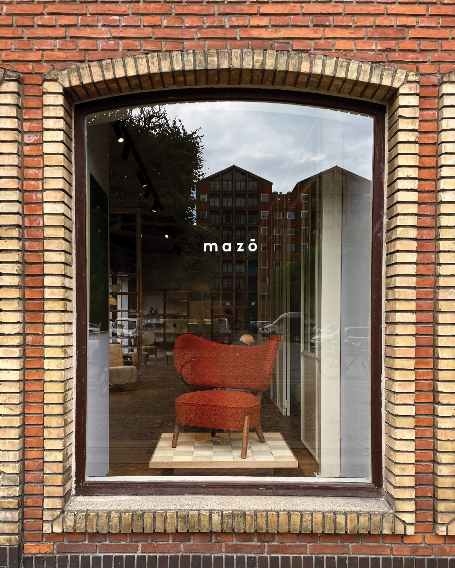 Mazo’s Copenhagen showroom window display with a rust-orange upholstered chair on a checkered plinth