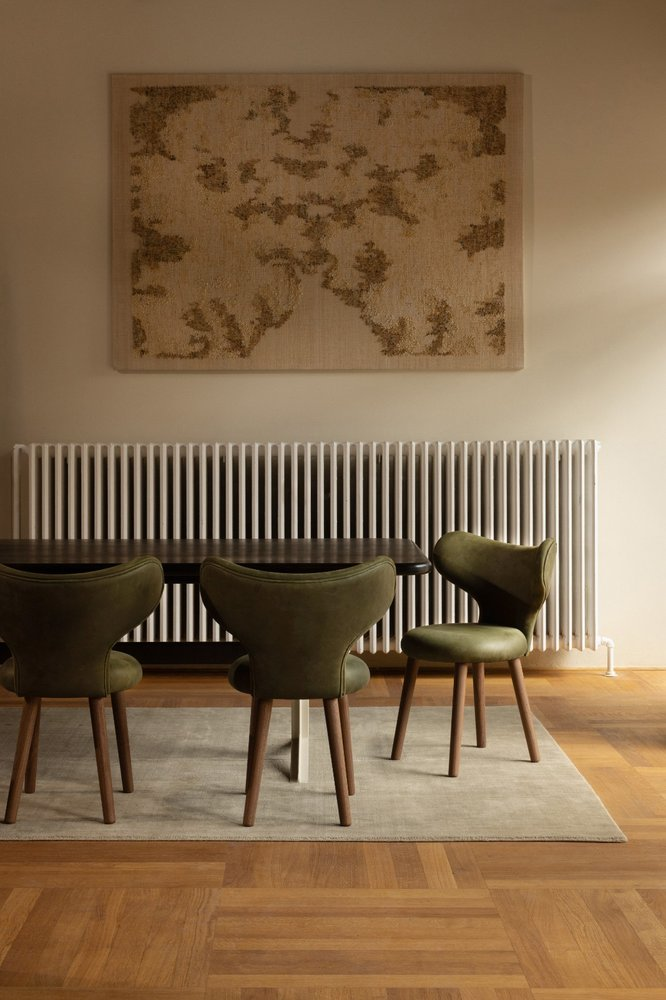 WNG Chairs in green leather around a dark dining table with a tapestry above