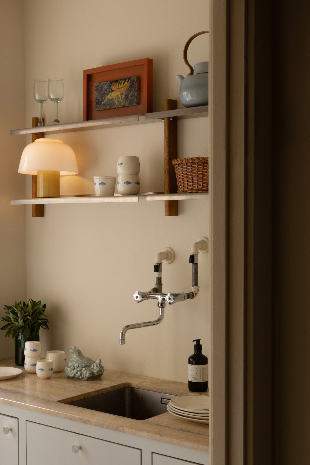 Two MOD wall shelves in oak and aluminium above a kitchen sink with a lit table lamp