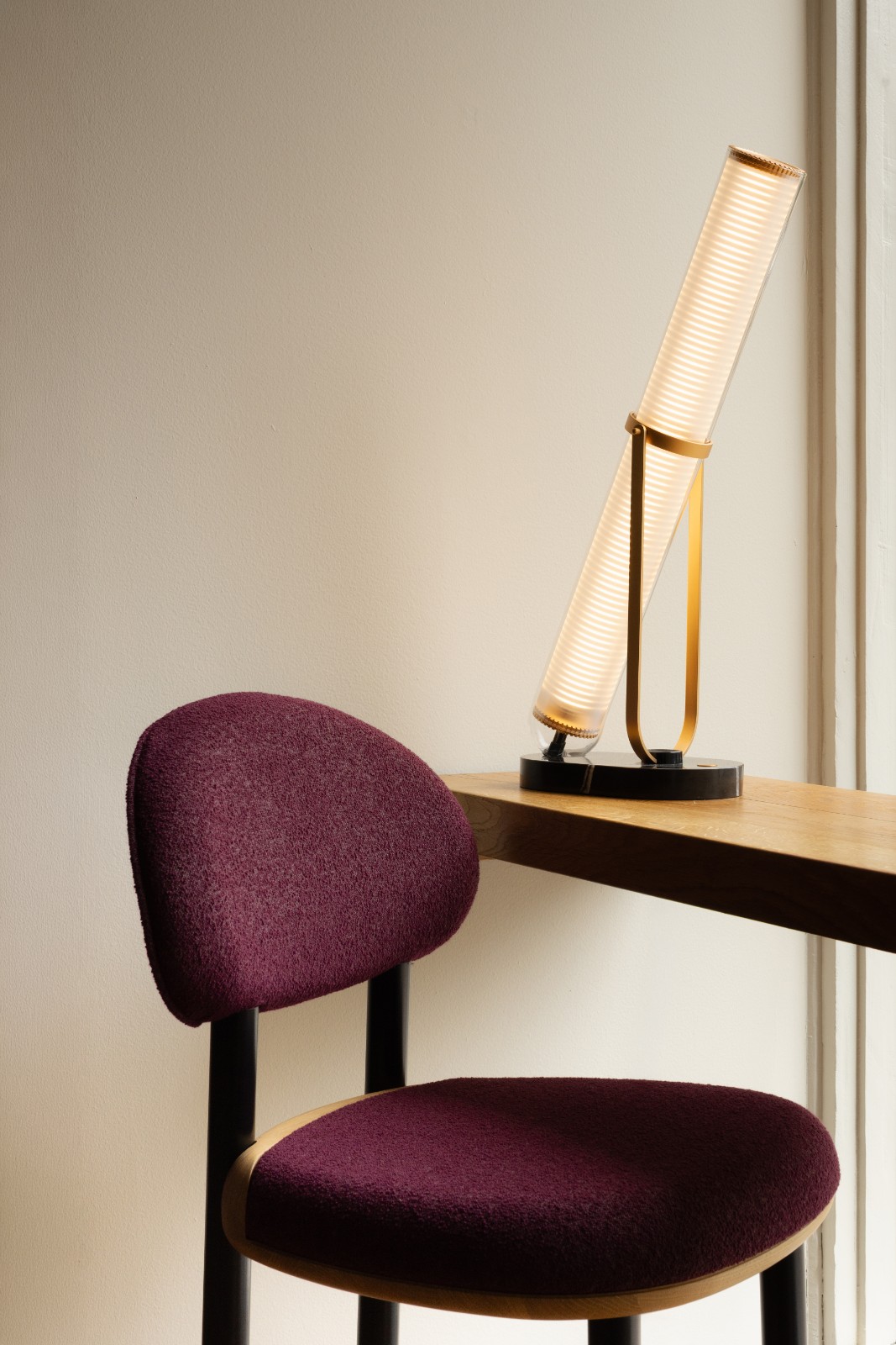 MAG Counter Chair in burgundy upholstery beside a glowing tube lamp on a wooden counter