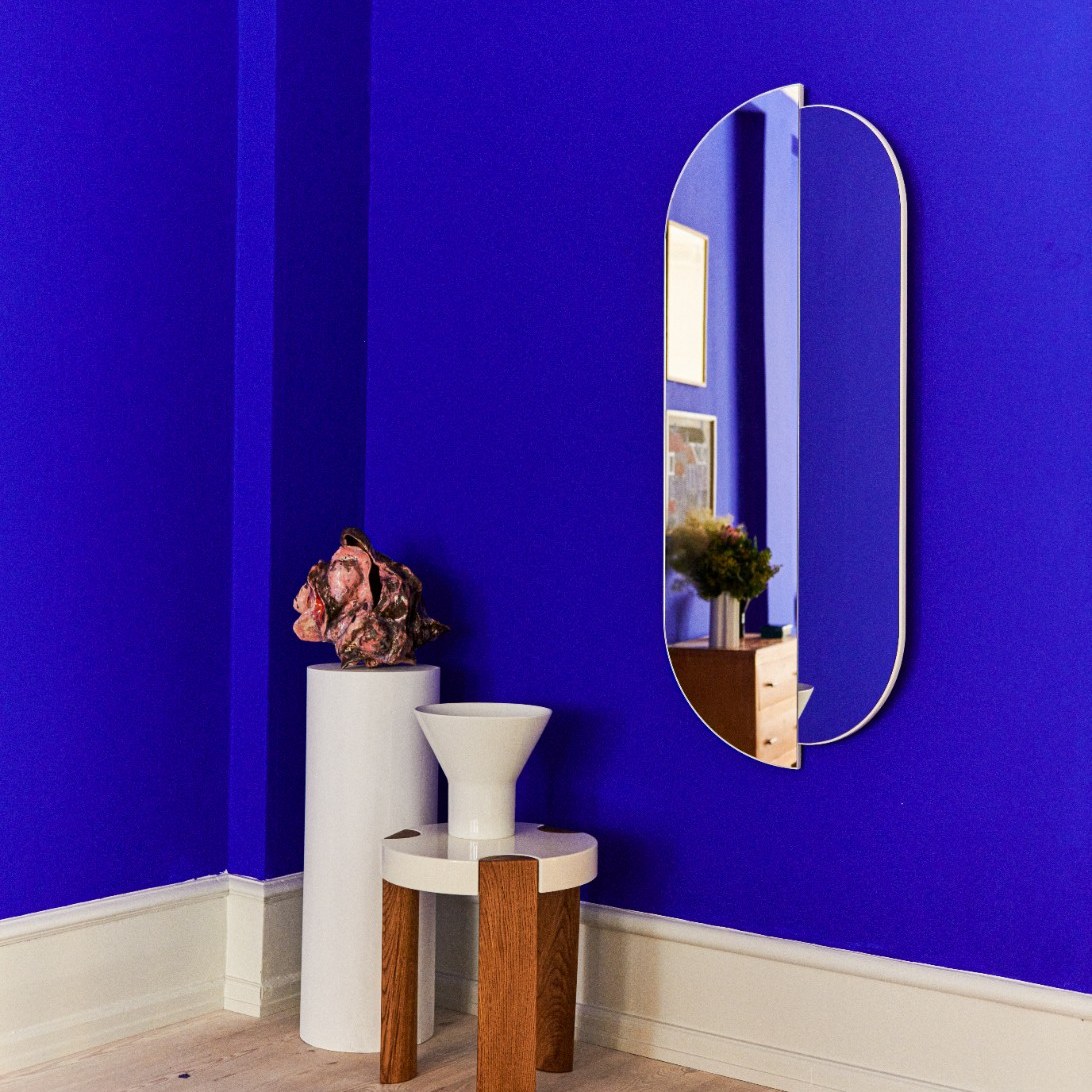 FER Side Table in white with oak legs against a blue wall beside a pedestal and a mirror